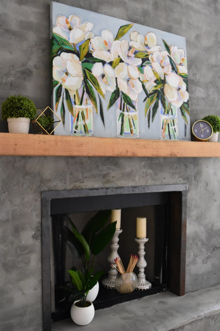 magnolia painting on modern concrete fireplace with wooden mantle.