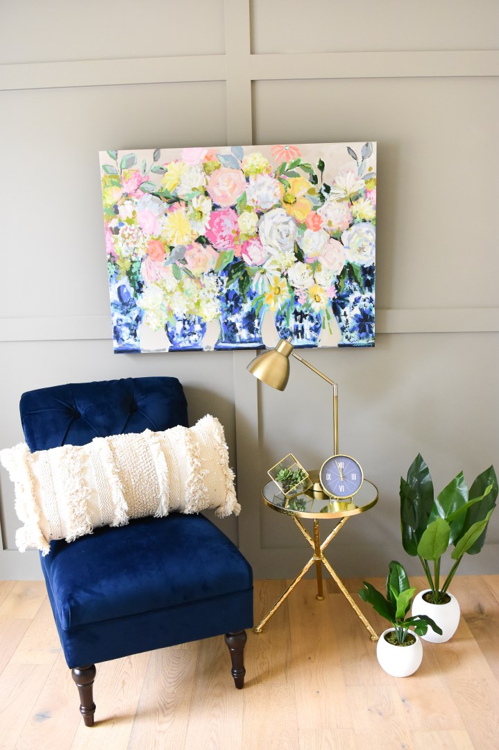Bright floral painting in blue and white ginger jars with blue accent chair and gold side table.