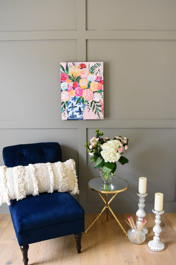 blush pink floral painting paired with a blue accent chair and gold side table.