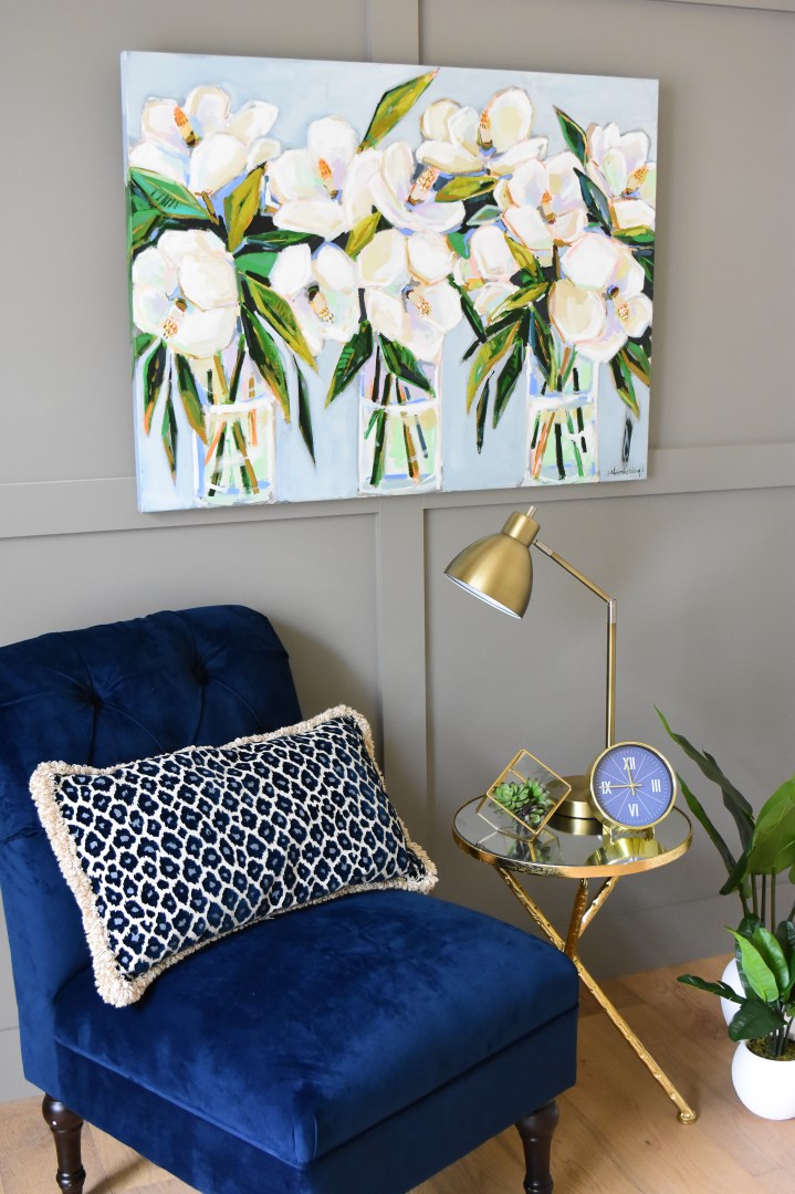 magnolia painting styled with blue background styled with blue velvet chair and gold side table.
