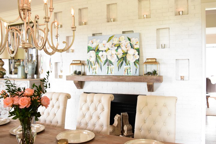 floral painting on mantle with gold chandelier and tufted chairs